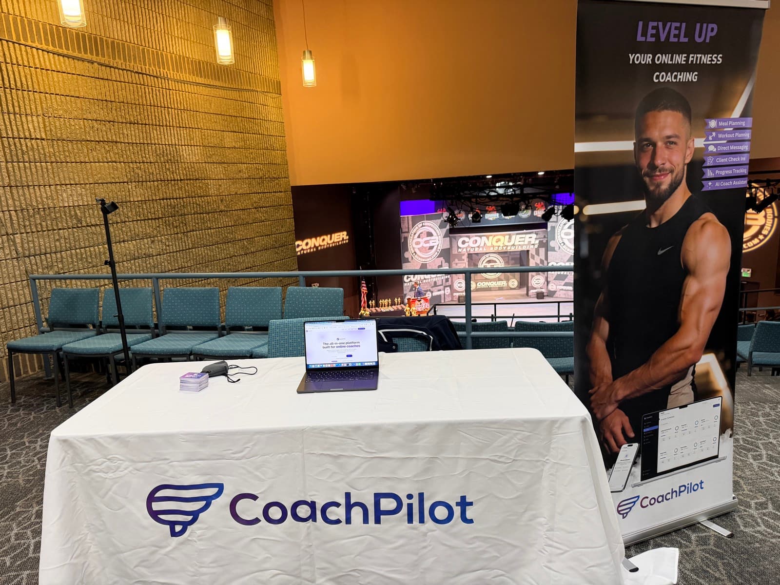 The CoachPilot table and banner at OCB The Conquer natural bodybuilding show, with the stage in the background